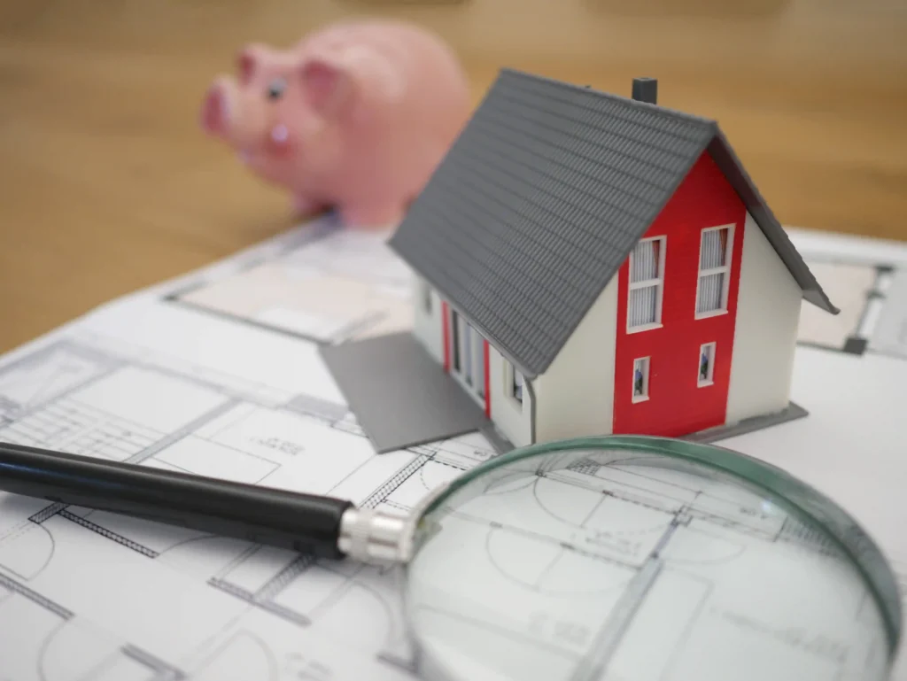 small model house with a piggy bank and magnifying glass beside it.